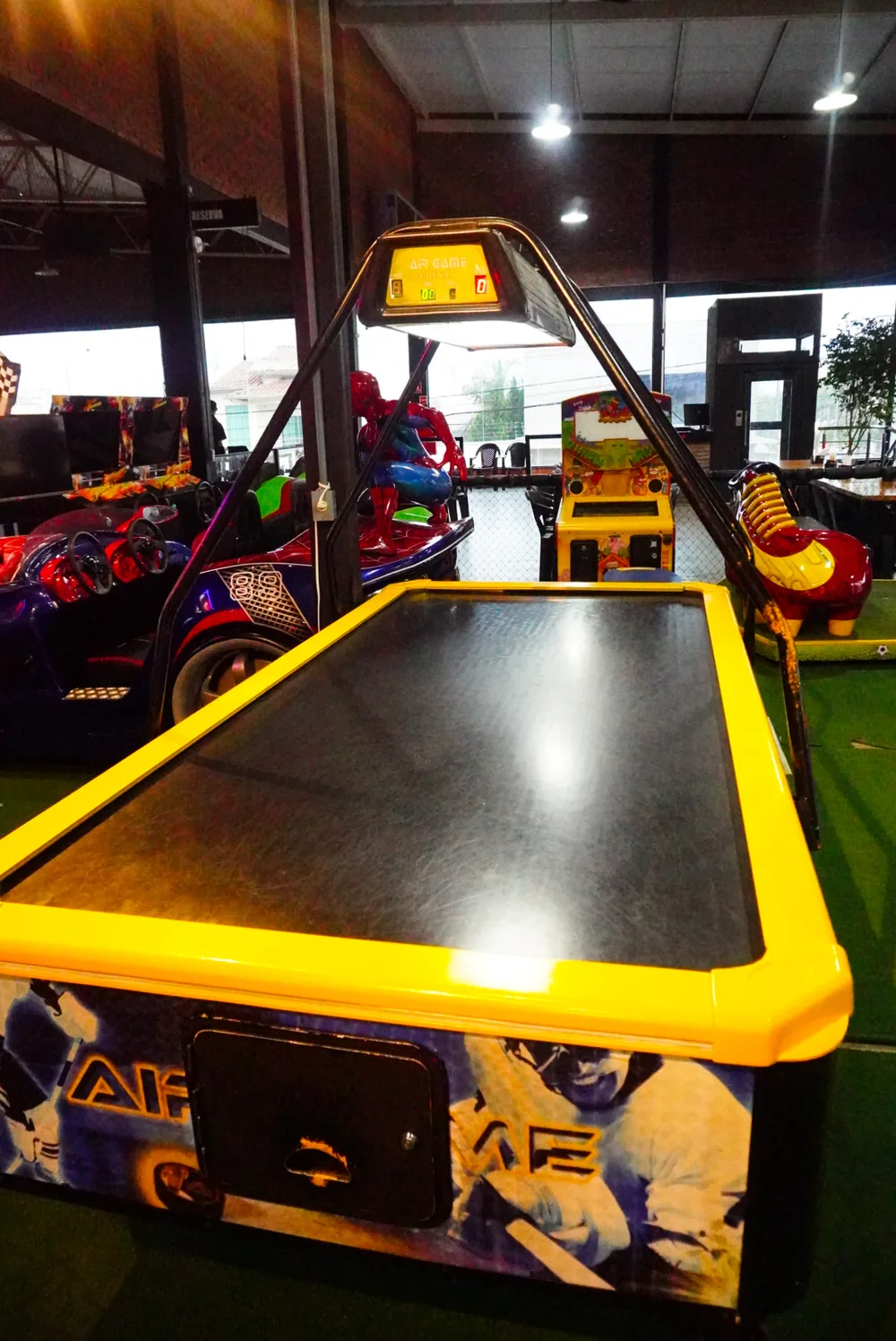 Espaço de brinquedos da Pizza Gyn — air hockey, carrinhos elétricos e área segura à vista da mesa