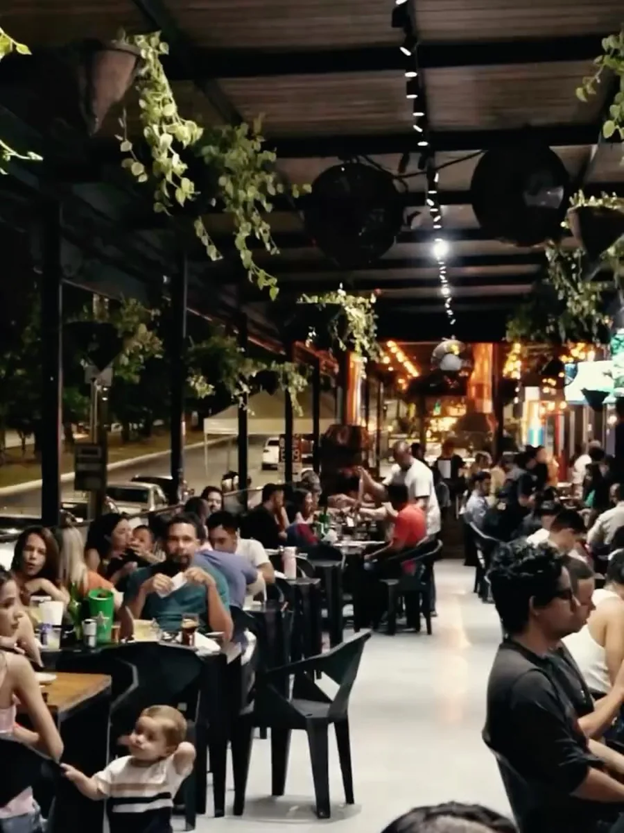 Salão da Pizza Gyn cheio, com plantas suspensas e luzes