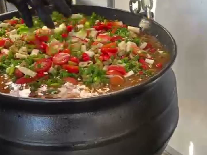 Caldeirão de ferro cheio de carreteiro fumegante, finalizado com tomate, pimenta e cebolinha, preparado ao vivo